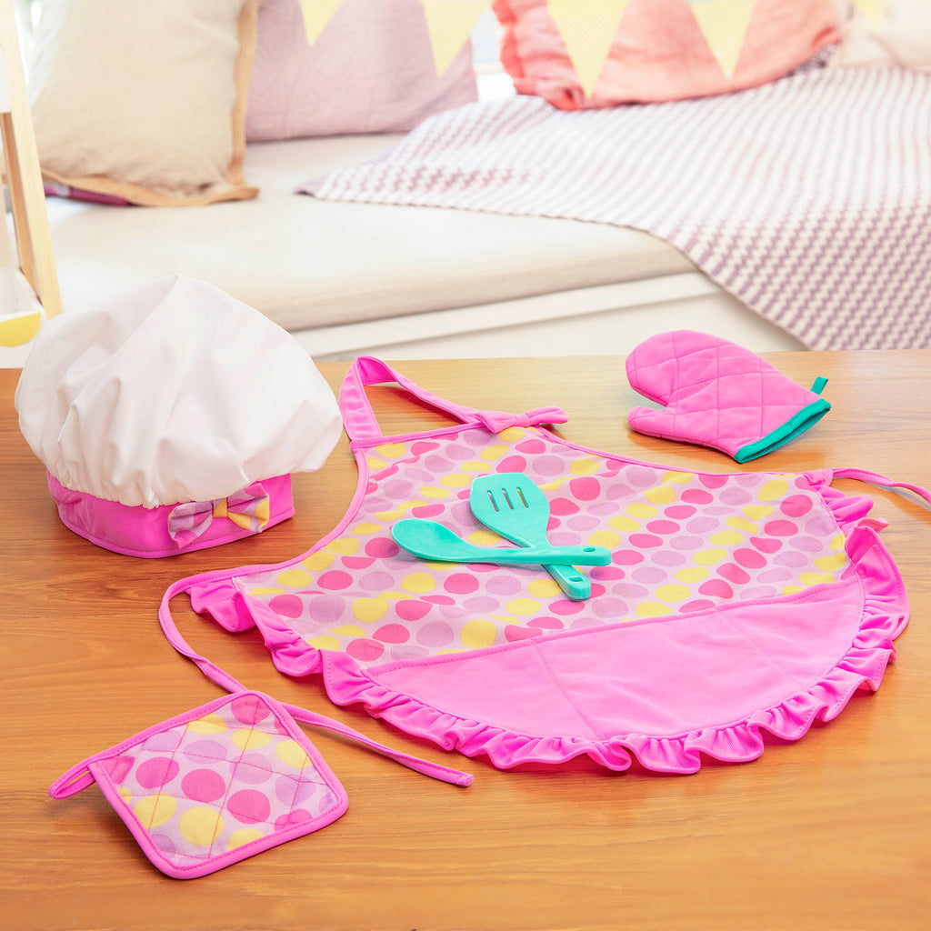 A pink apron set for kids with a chef's hat, oven mitt, and more.IThe Smart Cookie Chef's Apron in a realistc setting, there is an apron, chef's hat, oven mitt, cooking utensils and pot holder.